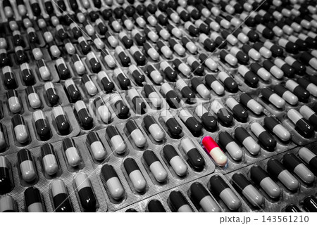 Red and white capsule among black and white capsules in overlapping blister packs, with individual compartments and silver foil backing, pharmaceutical packaging for oral medicine and pharmacy supply. Red and white capsule among black and white capsules in overlapping blister packs, with individual compartments and silver foil backing, pharmaceutical packaging for oral medicine and pharmacy supply. 143561210