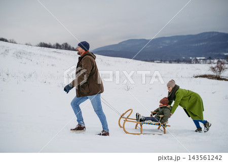 Happy family enjoying sledding together in snowy winter countryside. 143561242