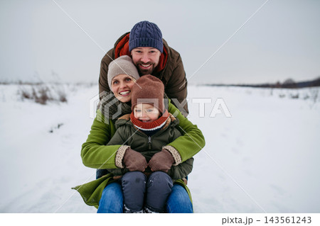 Happy family enjoying sledding together in snowy winter countryside. Happy family enjoying sledding together in snowy winter countryside. 143561243