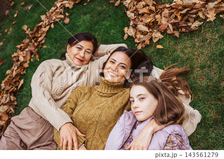 Mother, grandmother and daughter, laying on grass in the middle of heart from leaves. 143561279