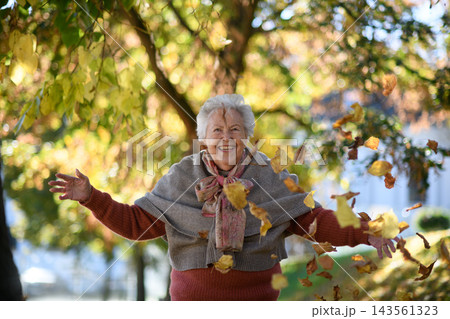 Portrait of elderly woman on walk in the park during warm autumn day, throwing colorful leaves. Portrait of elderly woman on walk in the park during warm autumn day, throwing colorful leaves. 143561323