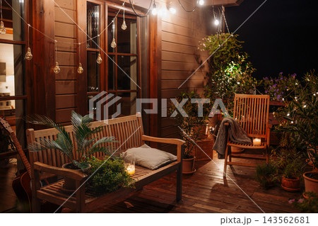 Cozy illuminated home terrace with seating during peaceful summer evening. Cozy illuminated home terrace with seating during peaceful summer evening. 143562681