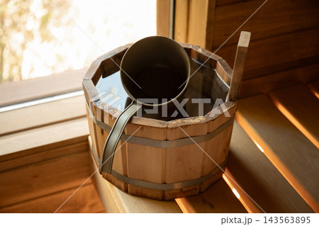 Wooden bucket filled with water sits beside a cup in tranquil sauna Wooden bucket filled with water sits beside a cup in tranquil sauna 143563895