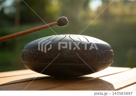 Musician strikes steel tongue drum with mallet, creating soothing sounds Musician strikes steel tongue drum with mallet, creating soothing sounds 143563897