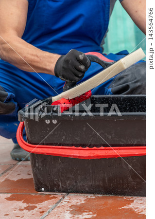 Close-up of gloved worker cleaning tile floor with scrub tool 143564766