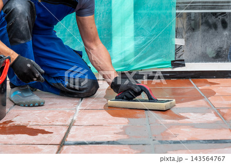 Worker kneeling and scrubbing wet terracotta floor tiles indoors Worker kneeling and scrubbing wet terracotta floor tiles indoors 143564767