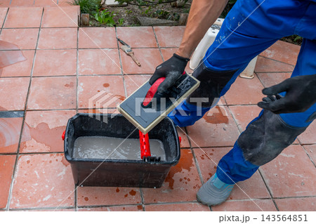 Worker applying grout on tiled floor with hand tools outdoors 143564851