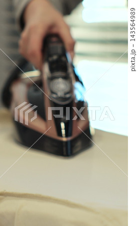 Vertical video. Woman using iron with steam mode for clothes. Home Routine Housekeeping. Vertical video. Woman using iron with steam mode for clothes. Home Routine Housekeeping. 143564989
