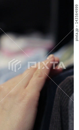 Vertical video. Woman hand runs across a rack of clothes at house or store. Home wardrobe or clothing shop changing room. Vertical video. Woman hand runs across a rack of clothes at house or store. Home wardrobe or clothing shop changing room. 143564999