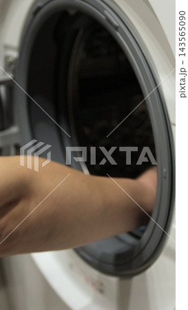 Vertical video. Woman pulls clean washed clothing from the washing machine. Washing clothing in domestic washing machine. 143565090
