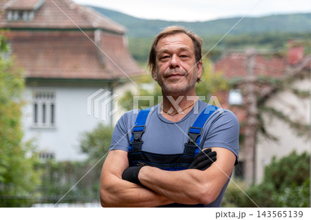 Confident handyman standing with crossed arms in a quiet village street 143565139