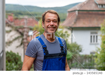 Smiling middle aged man standing outdoors with village houses behind 143565140