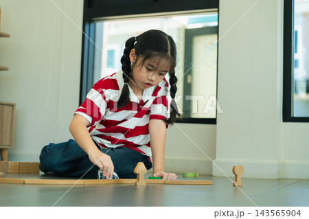 Young girl with braided hair wearing red and white striped shirt playing wooden block game on floor indoors Young girl with braided hair wearing red and white striped shirt playing wooden block game on floor indoors 143565904