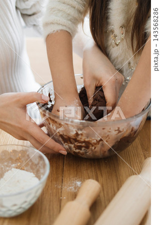 A mother and daughter are mixing dough in a glass bowl, preparing to bake cookies together in the kitchen A mother and daughter are mixing dough in a glass bowl, preparing to bake cookies together in the kitchen 143568286