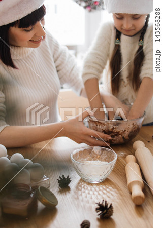A mother and daughter wearing Santa hats are happily mixing ingredients in a bowl for holiday baking A mother and daughter wearing Santa hats are happily mixing ingredients in a bowl for holiday baking 143568288