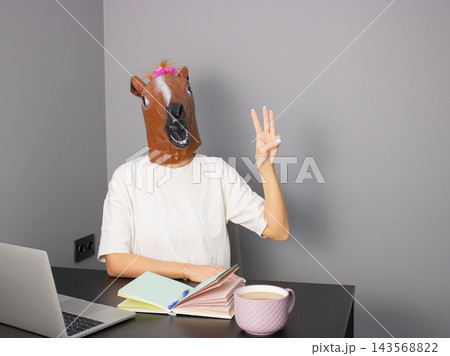 A Humorous Scene Featuring a Person with a Horse Mask Engaging in a Quirky Work Environment with Writing Tools and a Mug 143568822