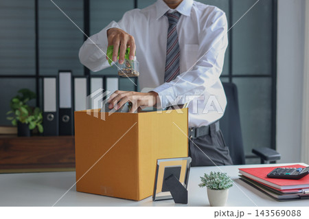 Office worker packing personal belongings into a cardboard box at a desk after job resignation or termination. 143569088