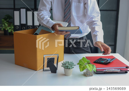 Male employee packing office desk items into box after job termination or resignation. Male employee packing office desk items into box after job termination or resignation. 143569089