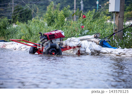 Pathum Thani Thailand - October 5 2026: A water pump engine setup alongside a sandbag barrier to drain floodwater from a submerged suburban road during severe seasonal flooding in Pathum Thani 143570125