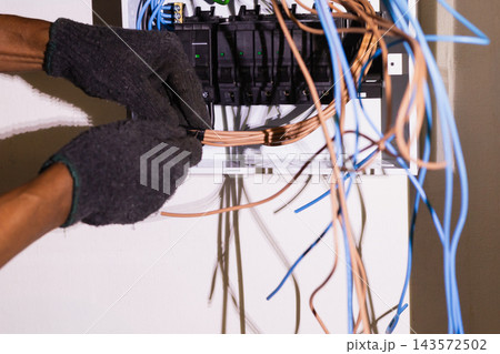 Electrician bundling and organizing electrical wires inside a circuit breaker. Electrician bundling and organizing electrical wires inside a circuit breaker. 143572502