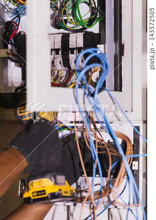 Electrician using an electric screwdriver to secure wires inside an electrical circuit. Electrician using an electric screwdriver to secure wires inside an electrical circuit. 143572505