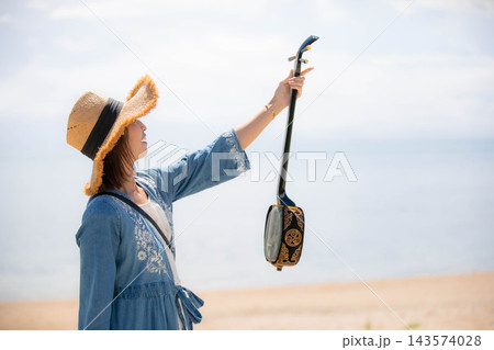 沖縄の海で三線を掲げる笑顔の女性モデル 沖縄の海で三線を掲げる笑顔の女性モデル 143574028