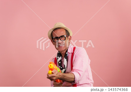 Senior man having fun with water gun on pink background Senior man having fun with water gun on pink background 143574368