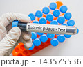 Gloved hand holding Bubonic Plague Test blood tube with laboratory rack 143575536