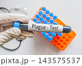 Gloved hand holding Plague Test blood tube with laboratory rack, infectious disease diagnostic testing concept 143575537