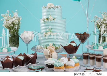 Three tiered mint birthday cake with cupcakes macarons and cake pops on dessert table 143576818