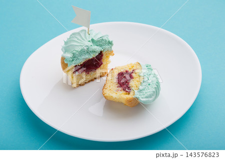 Cut in half cupcake showing rich berry jam filling with mint frosting on white plate 143576823
