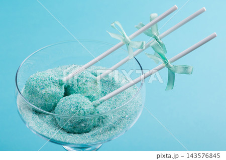 Close up of mint turquoise cake pops in sugar filled glass with satin bows on blue background Close up of mint turquoise cake pops in sugar filled glass with satin bows on blue background 143576845