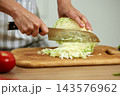 Hands cutting green cabbage with a sharp knife on a wooden cutting board, making a healthy vegetable salad 143576962