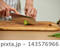 Chef hands preparing food, cutting fresh cucumber with a knife on a wooden chopping board in a modern kitchen 143576966