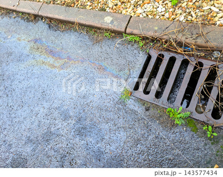 Oil spill from a petrol car on the road running down the drain pollution Oil spill from a petrol car on the road running down the drain pollution 143577434