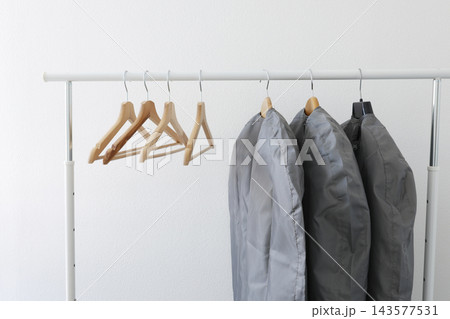 Garment storage bags protect seasonal clothes on rack with wooden hangers. Fabric care dry cleaning dust protection closet organization. Seasonal wardrobe change smart housekeeping. Garment storage bags protect seasonal clothes on rack with wooden hangers. Fabric care dry cleaning dust protection closet organization. Seasonal wardrobe change smart housekeeping. 143577531