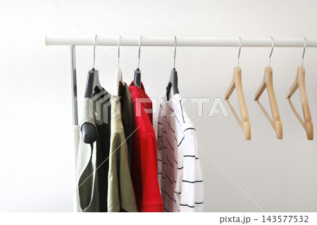 Basic casual t-shirts hang on home rack with empty wooden hangers in room. Sustainable lifestyle conscious organization simple living. Capsule closet declutter everyday routine. 143577532