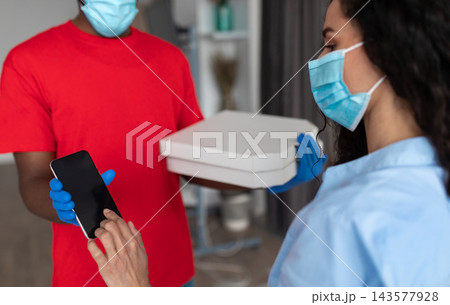 Courier Service, Safety Concept. Customer In Protective Medical Face Mask Signing Electronic Form Or Receipt After Receiving Order Using Mobile Phone, Delivery Guy Holding Cardboard Pizza Boxes 143577928