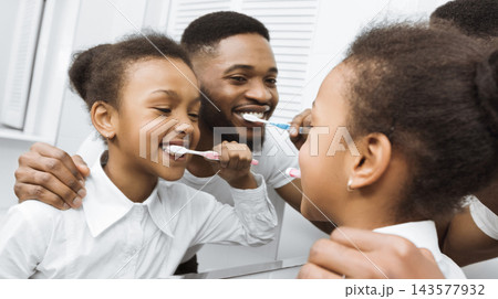 Little African American Daughter And Father Brushing Teeth Together In The Morning, Looking At Mirror Little African American Daughter And Father Brushing Teeth Together In The Morning, Looking At Mirror 143577932