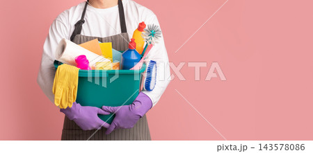 Bucket with cleaning supplies and tools in hands of unrecognizable man in apron standing on pink background, cropped image, panorana with free space Bucket with cleaning supplies and tools in hands of unrecognizable man in apron standing on pink background, cropped image, panorana with free space 143578086