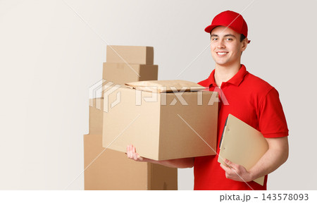 Courier and package in warehouse. Smiling deliveryman holding big box and tablet under his arm near stack of parcels, panorama, studio shot Courier and package in warehouse. Smiling deliveryman holding big box and tablet under his arm near stack of parcels, panorama, studio shot 143578093