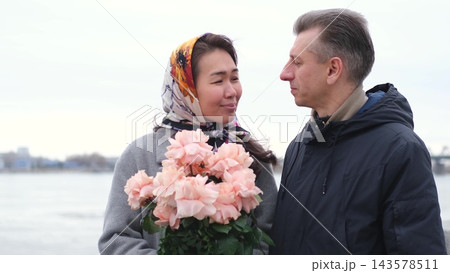 Mature couple kissing with a bouquet of roses by the river. Lasting love, intimacy and devotion. Mature couple kissing with a bouquet of roses by the river. Lasting love, intimacy and devotion. 143578511