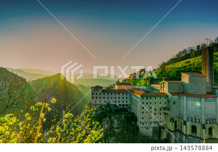 Stone buildings on a rocky mountainside in Spain at sunrise during spring, red tiled roofs and a church tower above a misty valley, green hills and distant mountain ridges beneath a clear morning sky 143578884