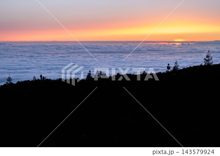 Warm sunset light spreads across a sea of clouds below the ridge in Teide National Park. Perspective and calm for wellbeing travel and mental reset campaigns. 143579924