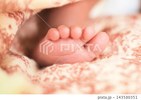 Tiny baby toes curl softly under a pastel blanket in an intimate closeup of newborn life. The photo suits themes of birth, innocence, parental bonding, child care, and emotional warmth. Tiny baby toes curl softly under a pastel blanket in an intimate closeup of newborn life. The photo suits themes of birth, innocence, parental bonding, child care, and emotional warmth. 143580351