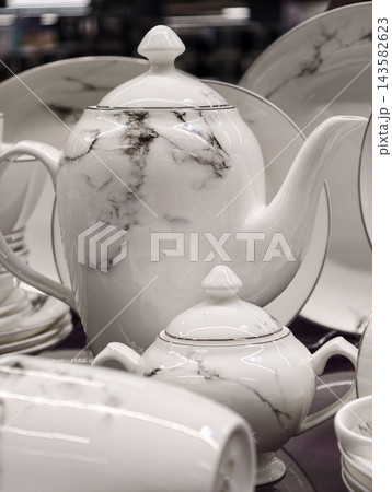 Luxury tall white porcelain teapot with marble inspired design forming an elegant high end tableware piece as part of refined premium dinner set for modern retail display Luxury tall white porcelain teapot with marble inspired design forming an elegant high end tableware piece as part of refined premium dinner set for modern retail display 143582623