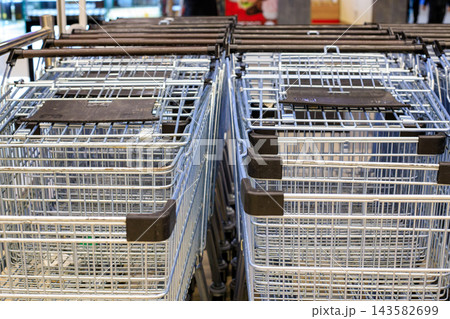 Rows of empty metal shopping trolleys under a canopy at the supermarket entrance. Neatly arranged metal shopping carts inside the supermarket. Overhead view. 143582699