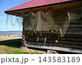 Old fishing nets hanging on a rustic log building with a red roof by White Sea, Russia. Traditional coastal fishing village scenery. Wooden cabin by the rocky shore and sea 143583189