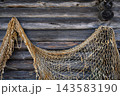 Close up of an old fishing net hanging on a weathered wooden log wall. Rustic maritime background with rough timber texture. Traditional fishing gear detail 143583190