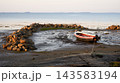 Small motorboat moored on a muddy tidal flat at low tide. Vessel secured near a stone breakwater on the rocky coast at White Sea, Russia. Nautical marine landscape 143583194